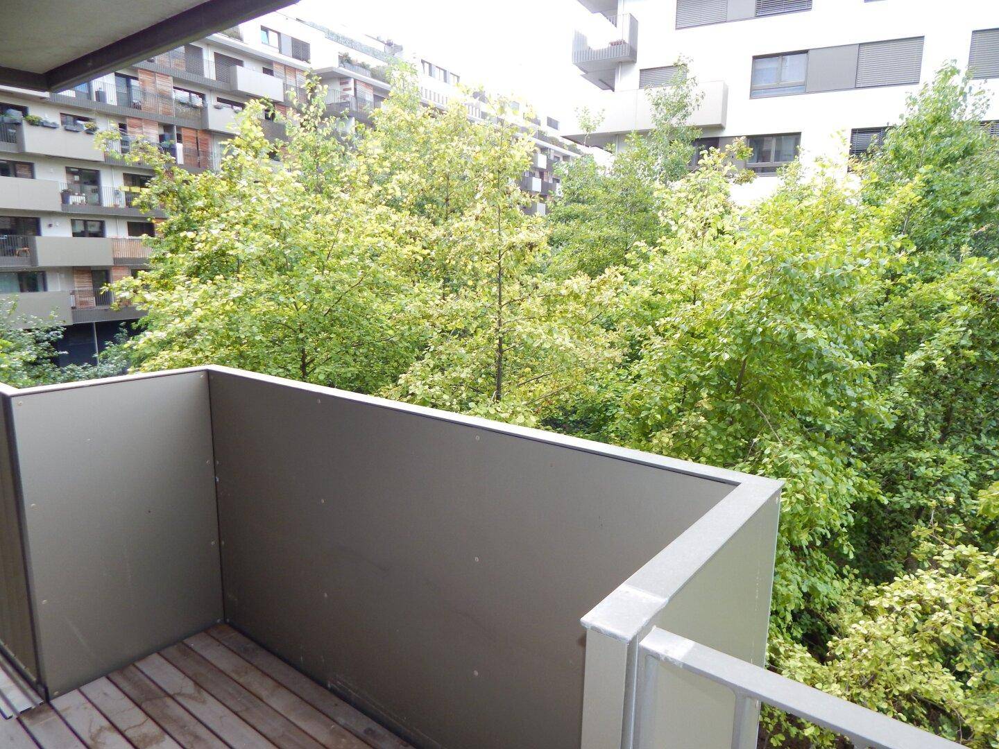 Balkon mit Holzboden und Blick auf den begrünten Innenhof und weitere Gebäude.