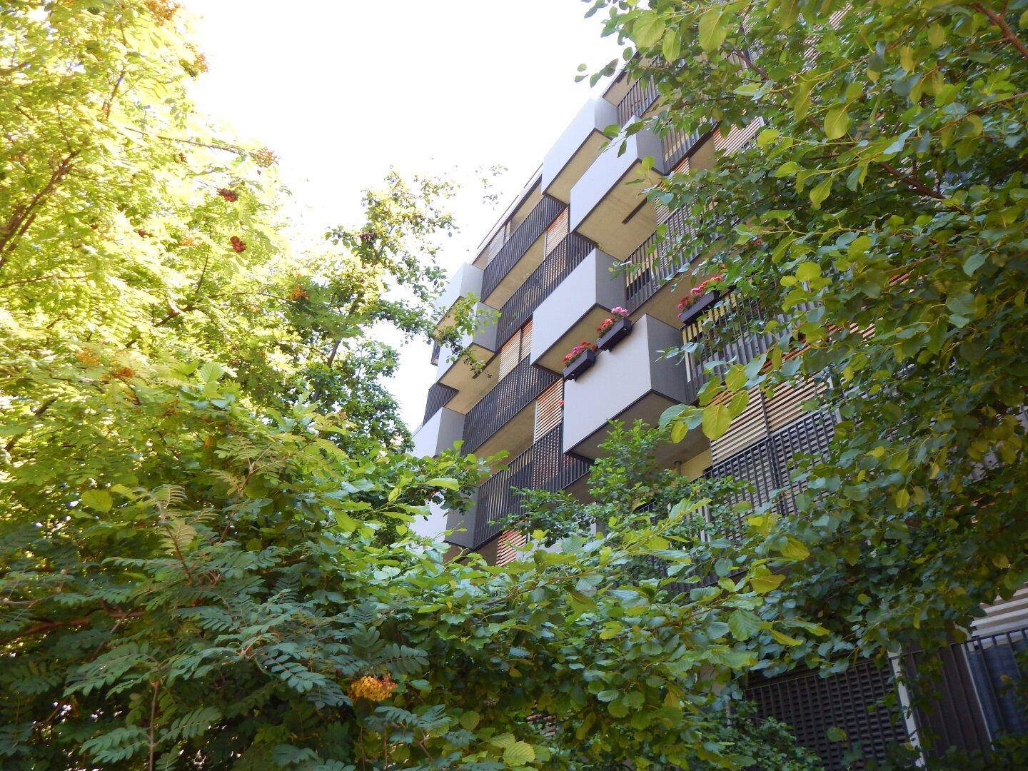 Moderne Gebäudefassade mit Balkonen, umgeben von üppigem Grün.