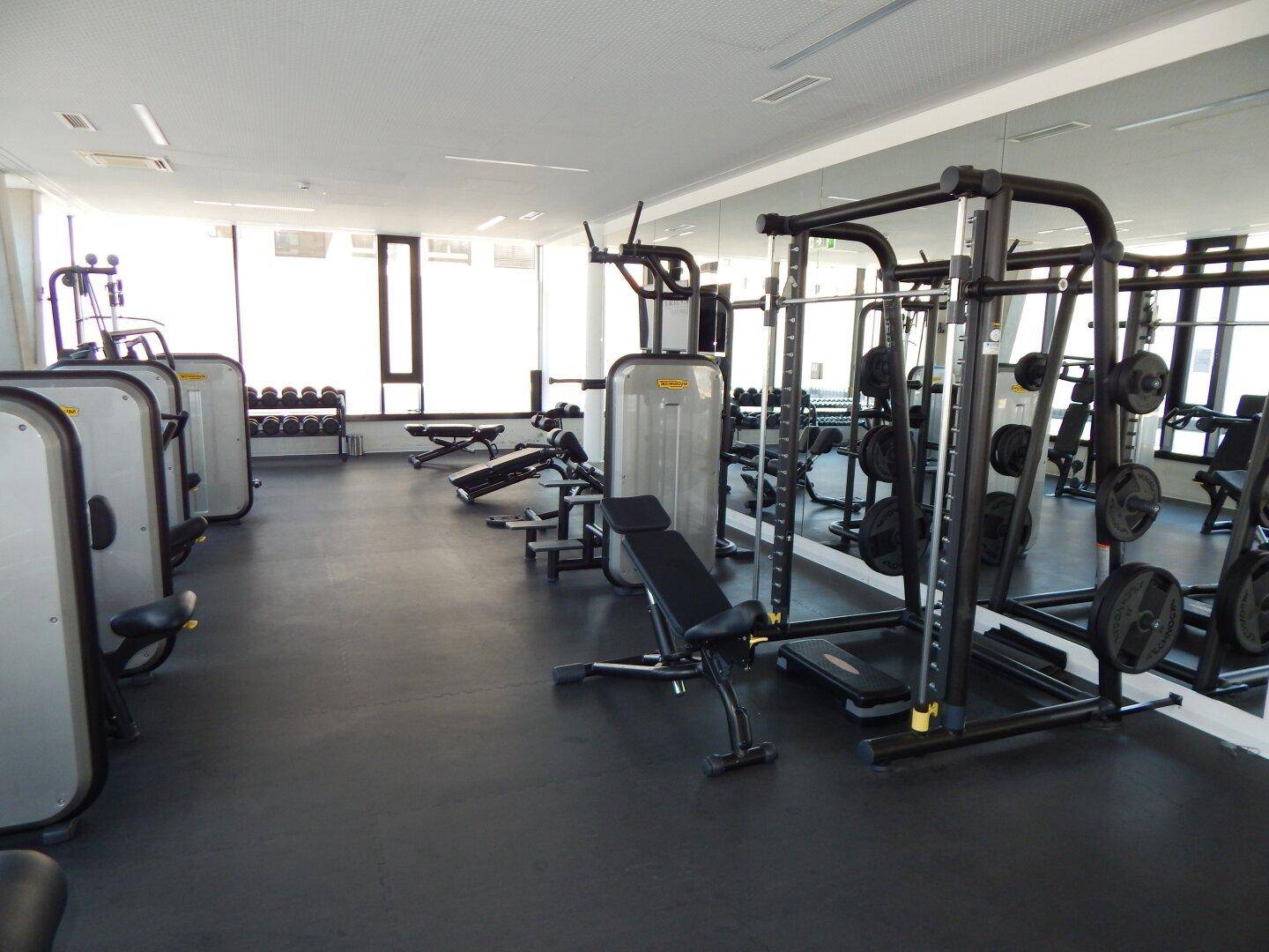 Gut ausgestatteter Fitnessraum mit Kraft- und Cardiogeräten sowie Spiegelflächen.