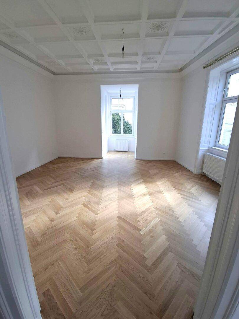 Geräumiges Zimmer mit Fischgrätparkett und einer beeindruckenden Kassettendecke, die den Altbaucharme unterstreicht.