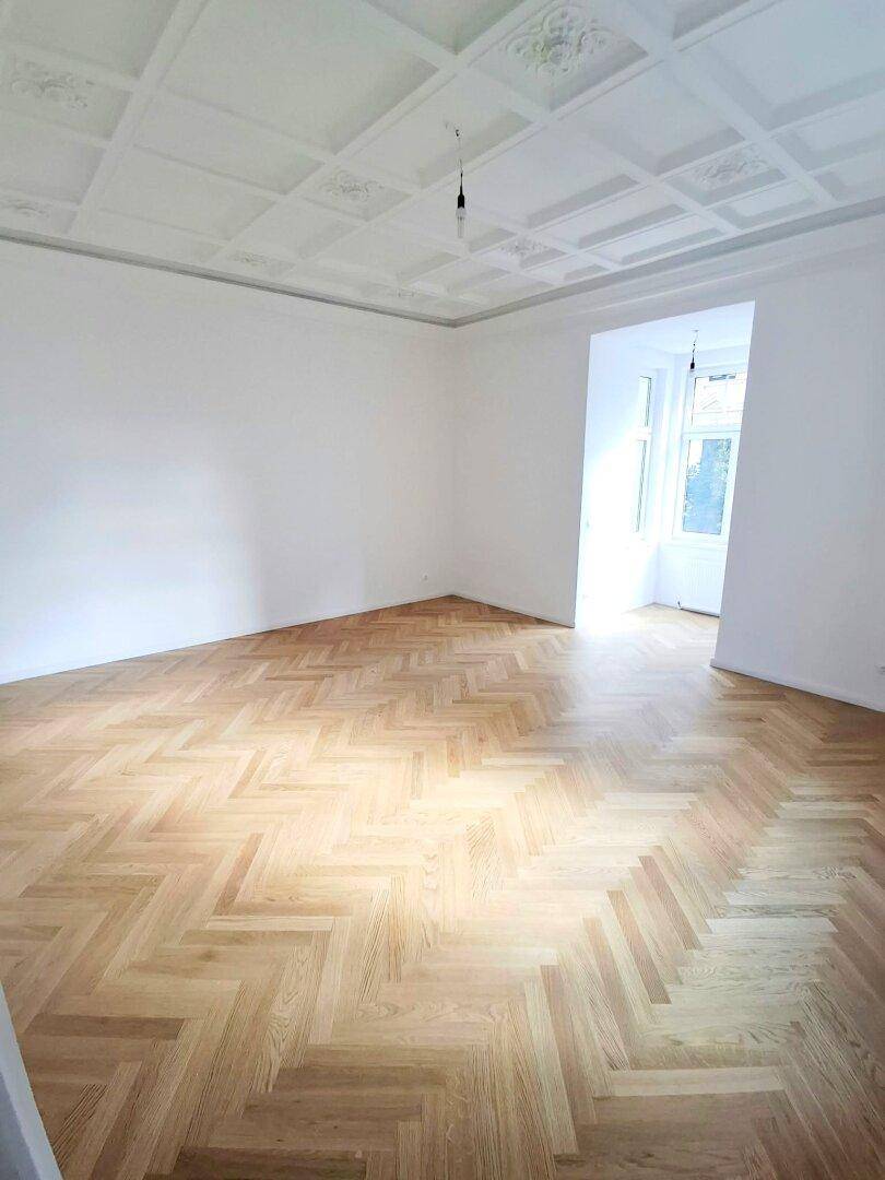 Großzügiger Raum mit Fischgrätparkett und einer detailreichen Kassettendecke, die für ein elegantes Ambiente sorgt.