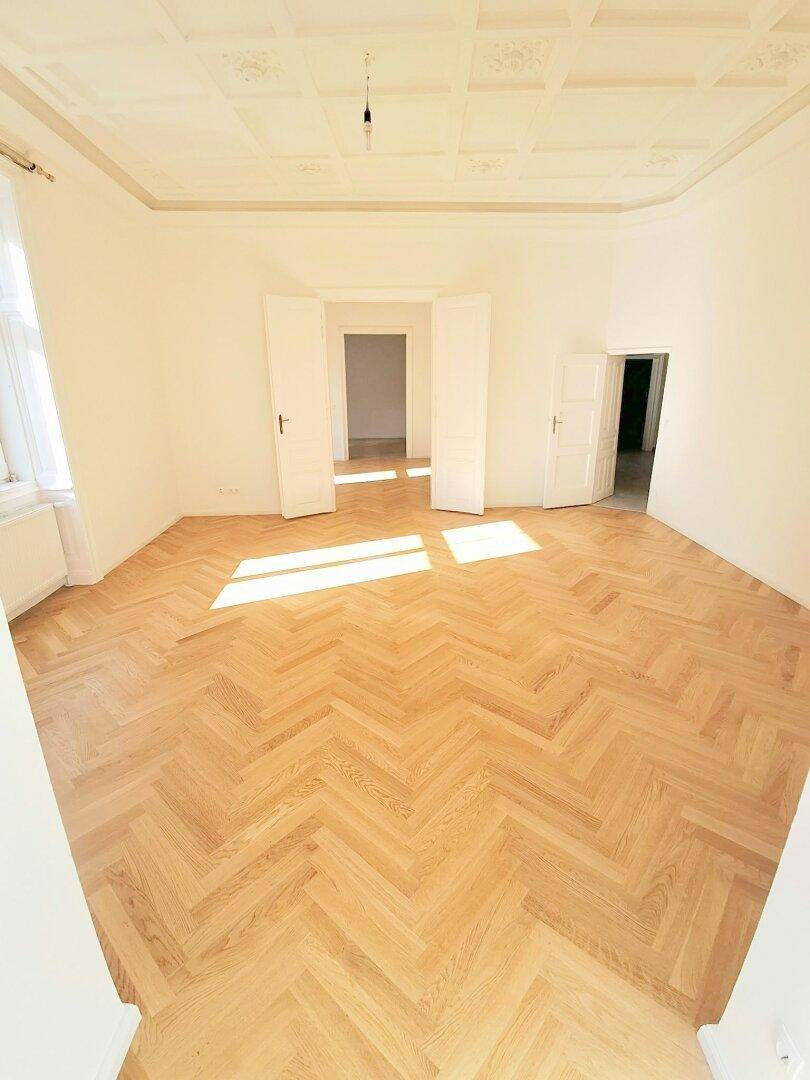 Heller Raum mit Fischgrätparkett und einer kunstvoll verzierten Kassettendecke, die Eleganz verleiht.