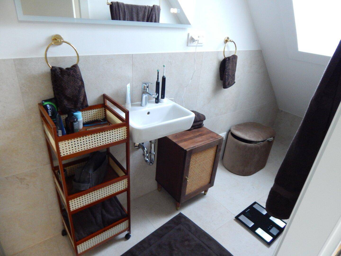 Badezimmer mit Einzelwaschbecken, Spiegelschrank und praktischem Rollwagen für Utensilien.