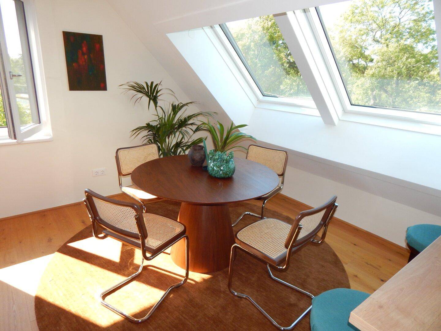 Gemütlicher Essbereich mit rundem Holztisch und Stühlen, hell durch große Fenster und Dachfenster.