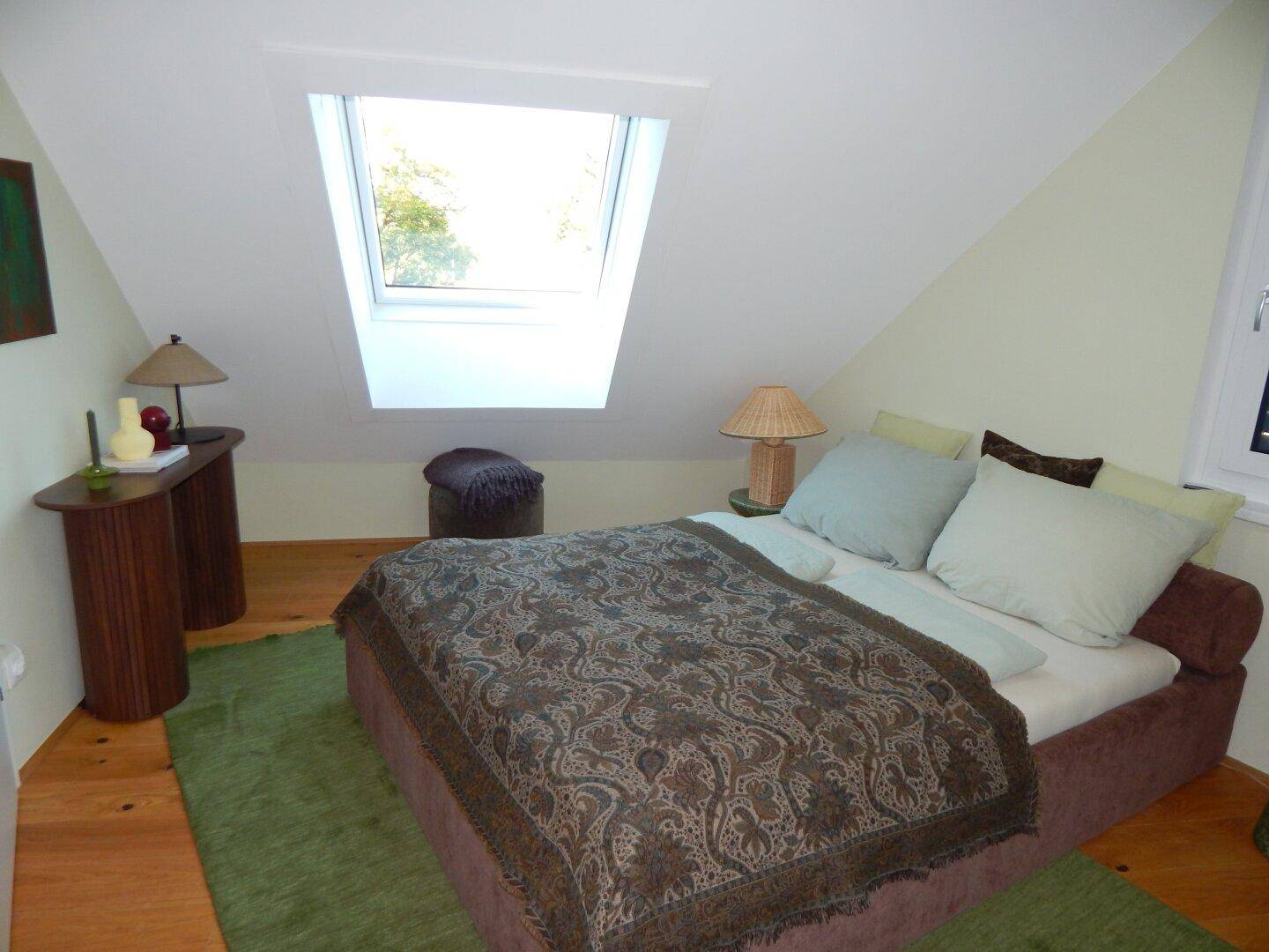 Helles Schlafzimmer mit Bett, Nachttischen und einem Dachfenster unter der schrägen Decke.