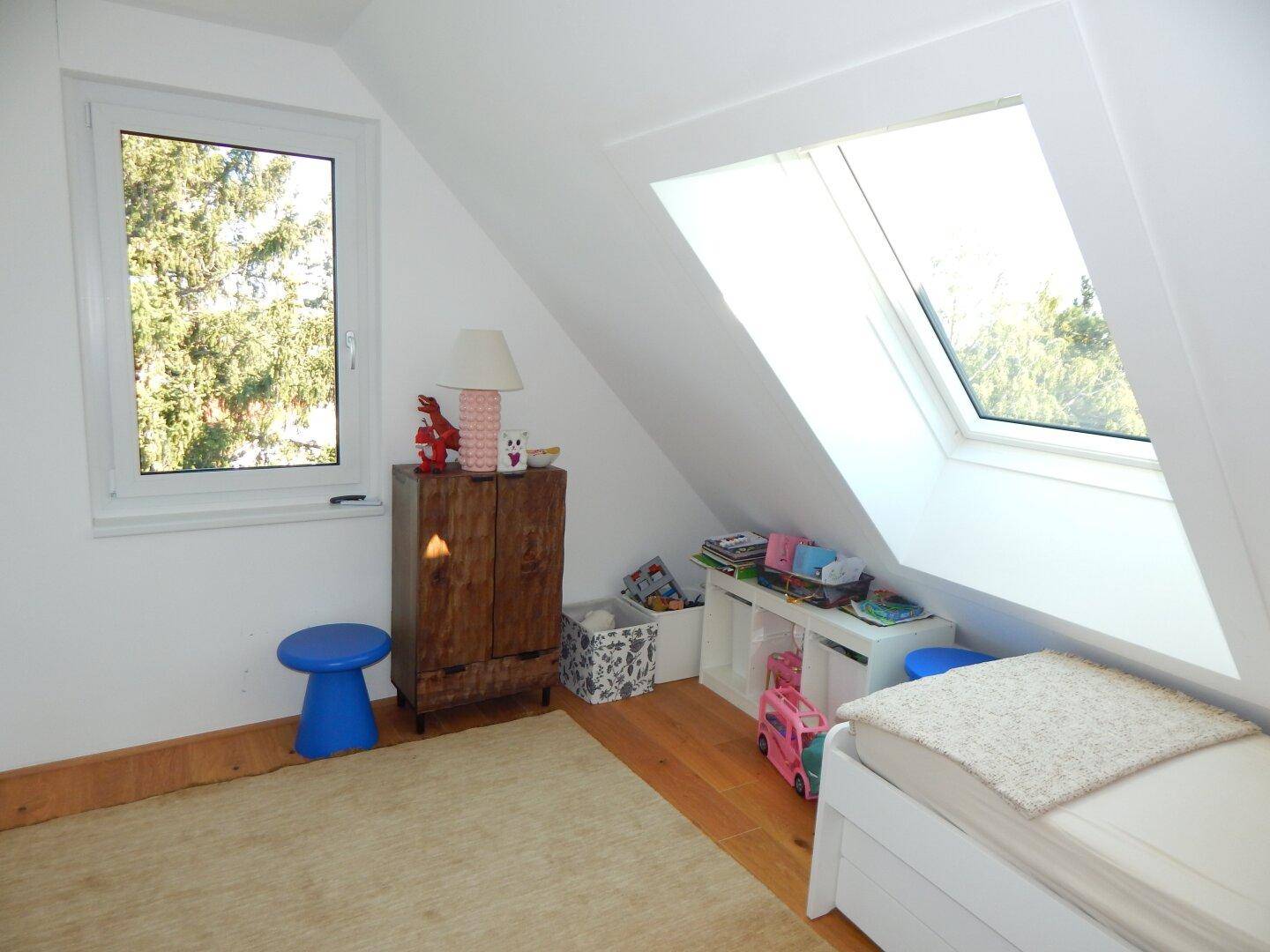 Helles Kinder- oder Gästezimmer mit Einzelbett, Schrank und einem Dachfenster.