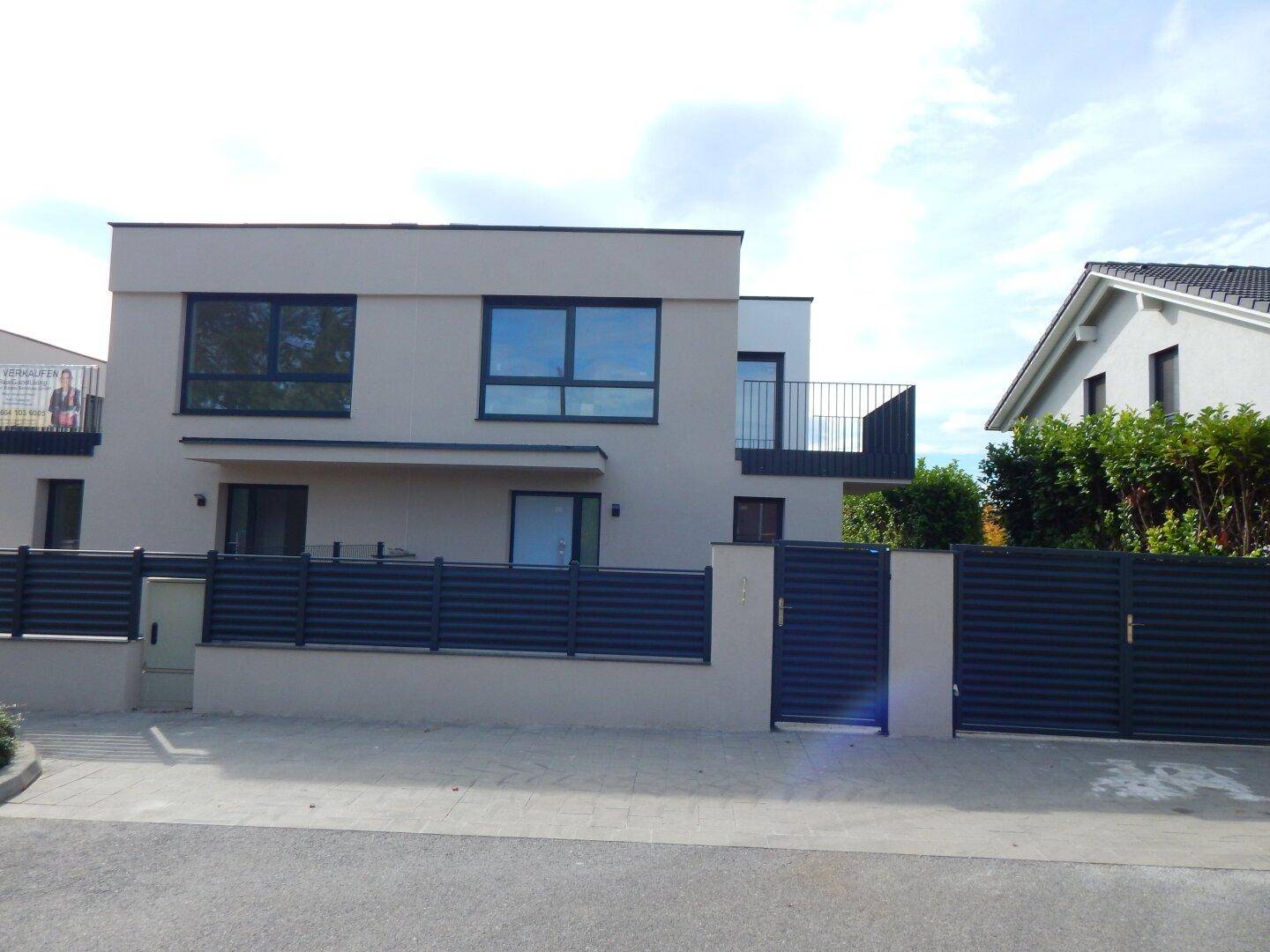 Moderne Doppelhaushälfte mit grauer Fassade und Zaun an der Straße.