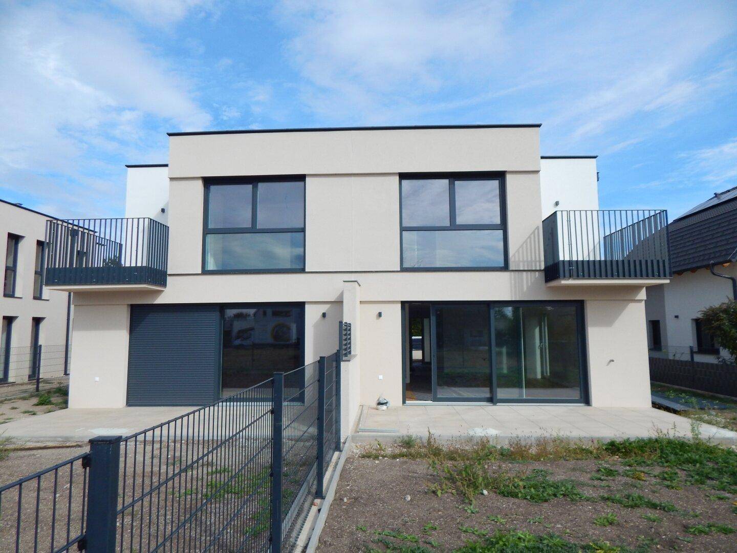 Frontansicht einer modernen Doppelhaushälfte mit Balkonen und Terrassenzugang.