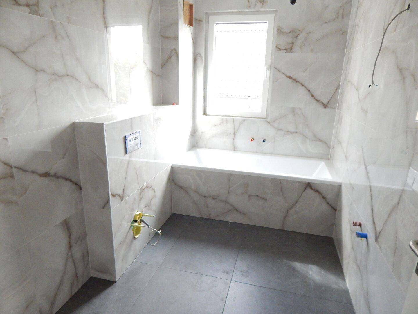 Modernes Badezimmer mit Marmorfliesen, Badewanne und Fenster für Tageslicht.