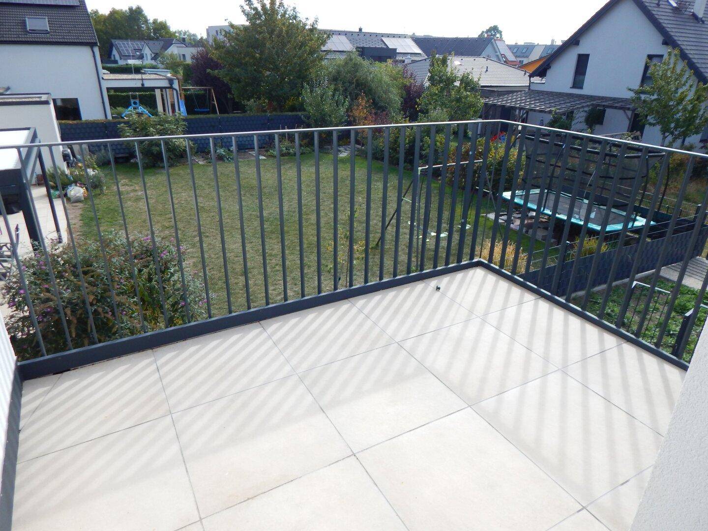 Geräumiger Balkon mit Fliesenboden und Blick auf den Gartenbereich.