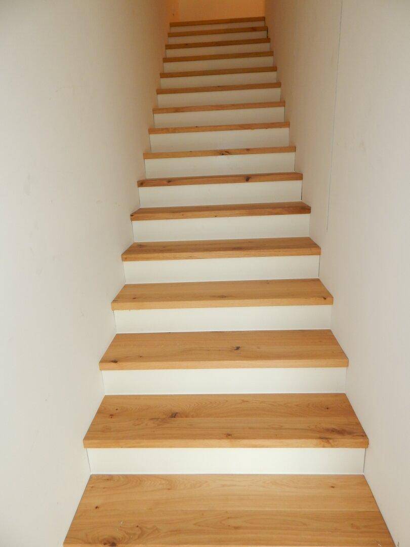 Moderne Holztreppe mit weißen Setzstufen, die die Stockwerke verbindet.