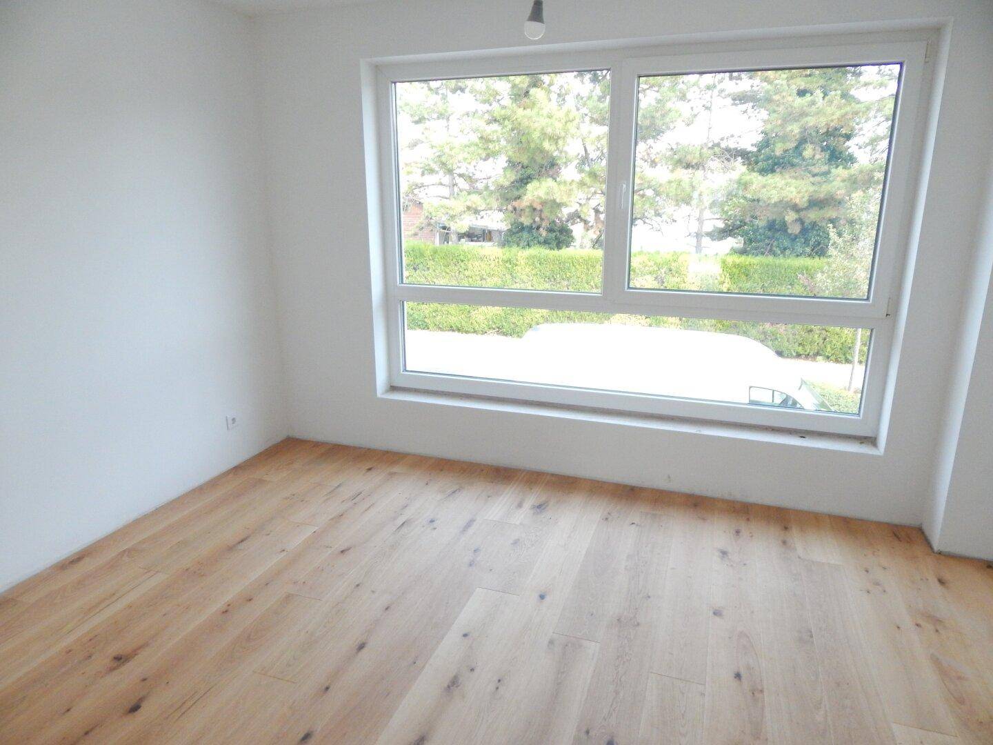 Helles Zimmer mit Holzboden und großem Fenster mit Blick ins Grüne.