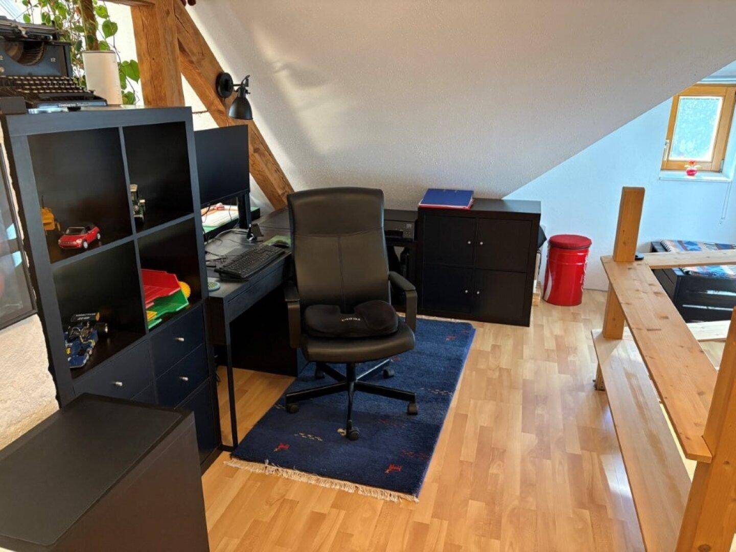 Arbeitszimmer im Dachgeschoss mit Schreibtisch, Bürostuhl und Regalen unter der Dachschräge.
