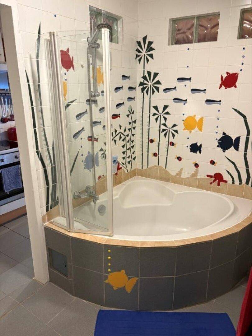 Badezimmer mit Eckbadewanne, Duschkabine und verspielten Fischmotiven an den Fliesen.