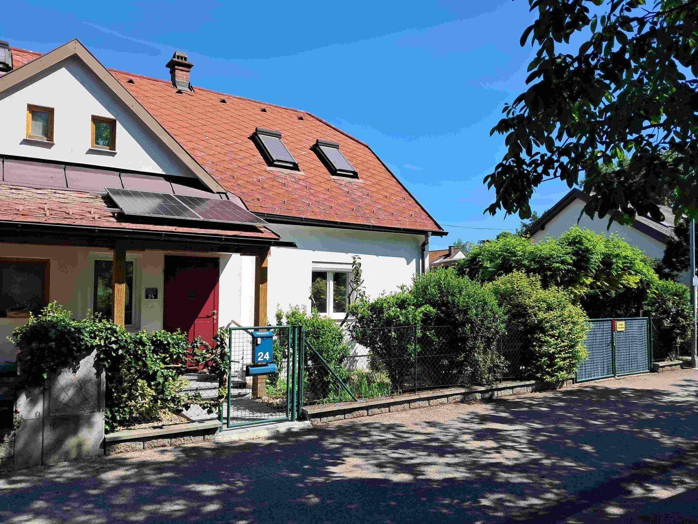 Einfamilienhaus mit rotem Ziegeldach, Solaranlage und gepflegtem Vorgarten unter blauem Himmel.