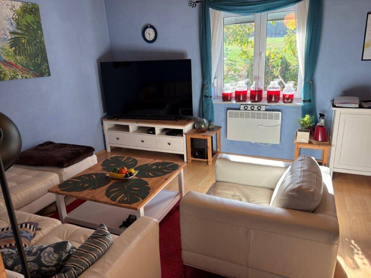 Helles Wohnzimmer mit blauen Wänden, Holzboden, Sofa und großem Fernseher.