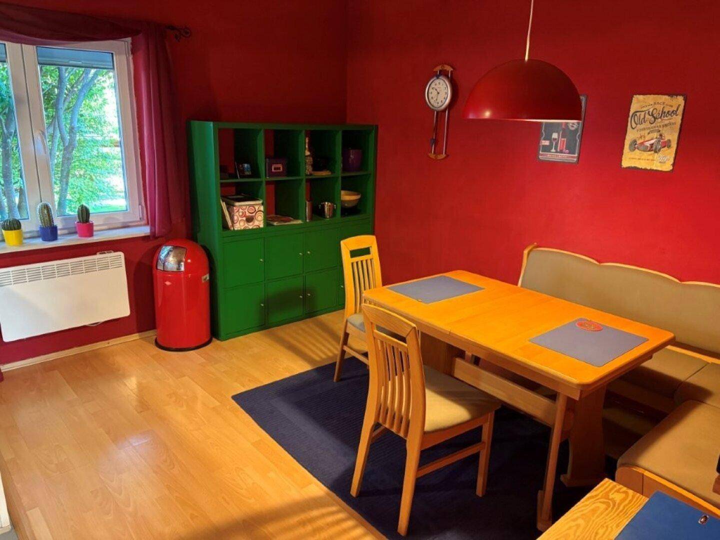Farbiges Esszimmer mit roter Wand, Holztisch, Sitzbank und Parkettboden.