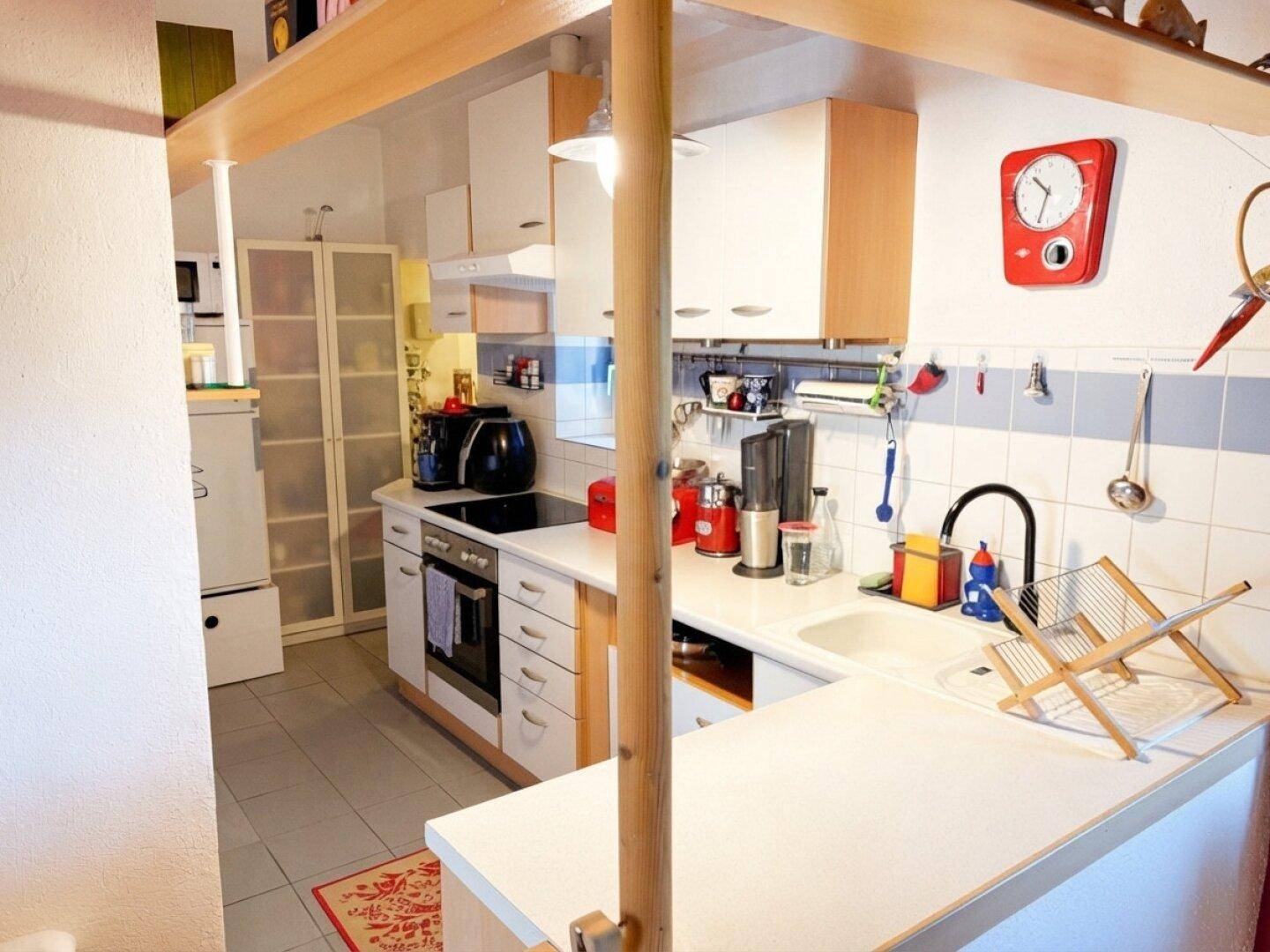 Funktionale Küche mit weißen Schränken, hellen Arbeitsplatten und Fliesenboden.