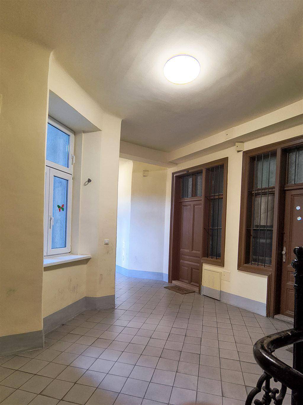 Heller Flur mit Fliesenboden, einem Fenster und mehreren Türen, der zu verschiedenen Wohnungen führt.