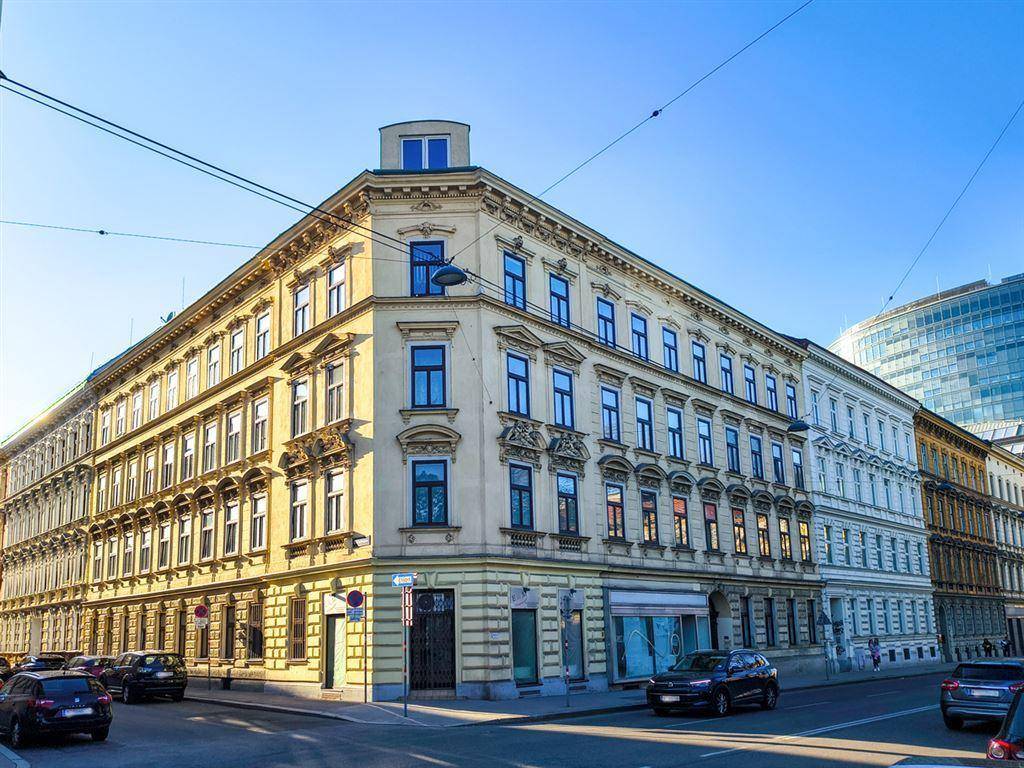 Historisches Eckgebäude mit detailreicher Fassade an einer belebten Straße unter klarem Himmel.