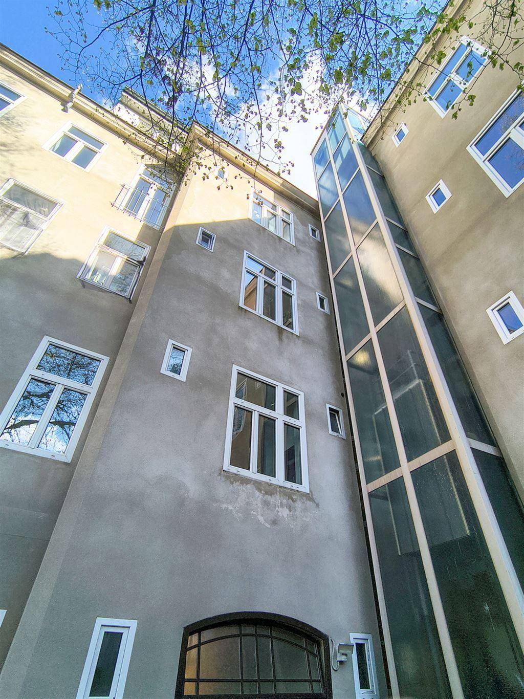 Gebäudefassade mit einem modernen Glasaufzug, der sich an die historische Architektur anfügt.