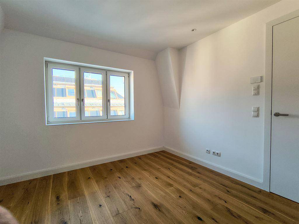 Helles Schlafzimmer mit Holzboden, weißen Wänden und einem Fenster, das viel Tageslicht hereinlässt.