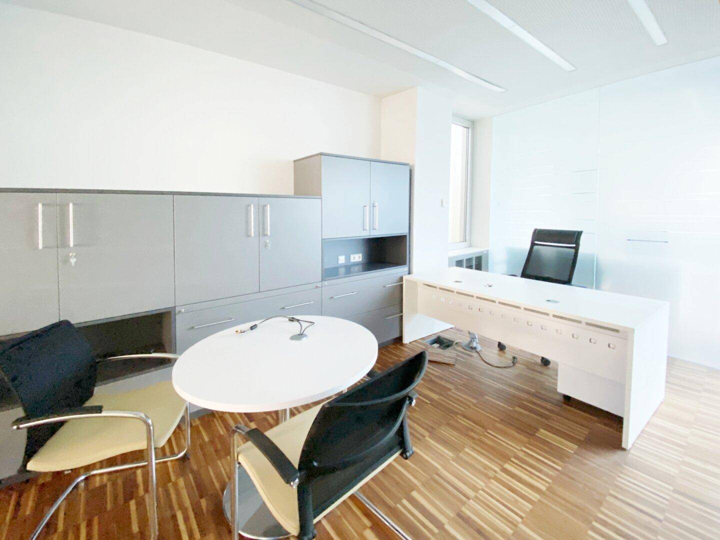Modern eingerichtetes Büro mit Holzparkett, weißen Wänden, grauen Schränken und einem großen weißen Schreibtisch.