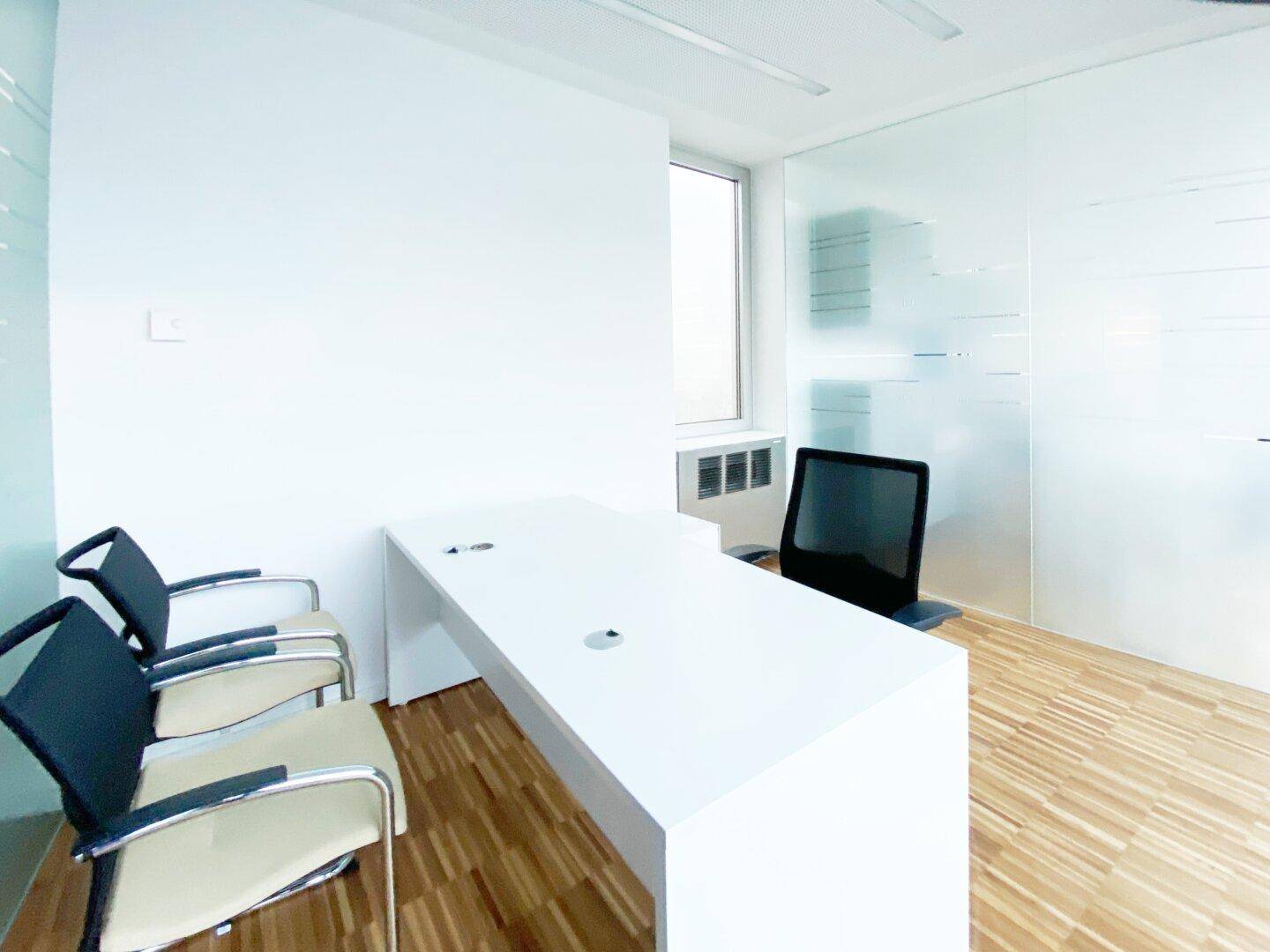 Helles Büro mit einem großen weißen Schreibtisch, ergonomischem Stuhl und einem Fenster, das viel Tageslicht hereinlässt.