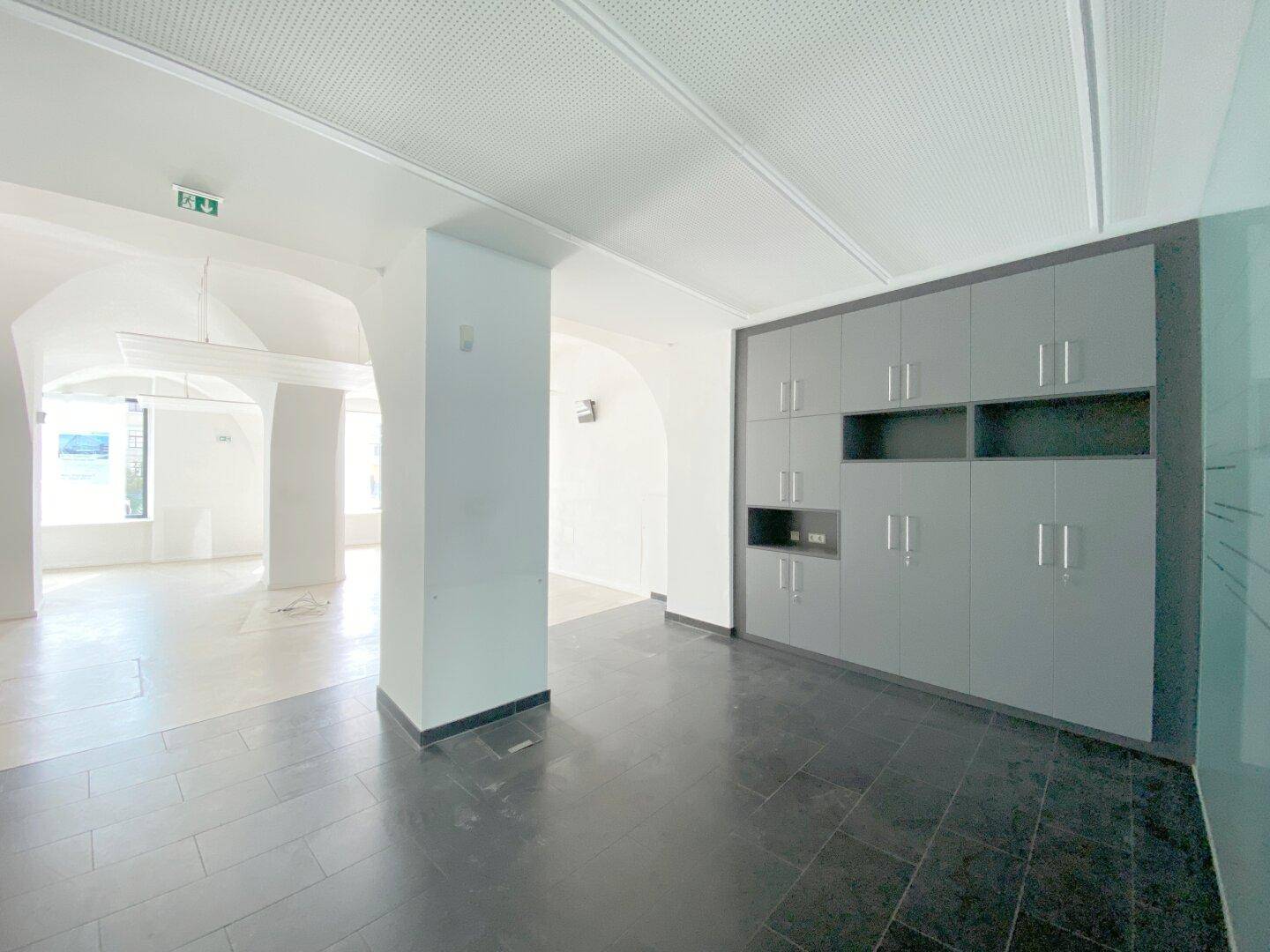 Bereich des Gewerberaums mit dunklen Fliesenböden und einer großen, grauen Einbauschrankwand für Stauraum.