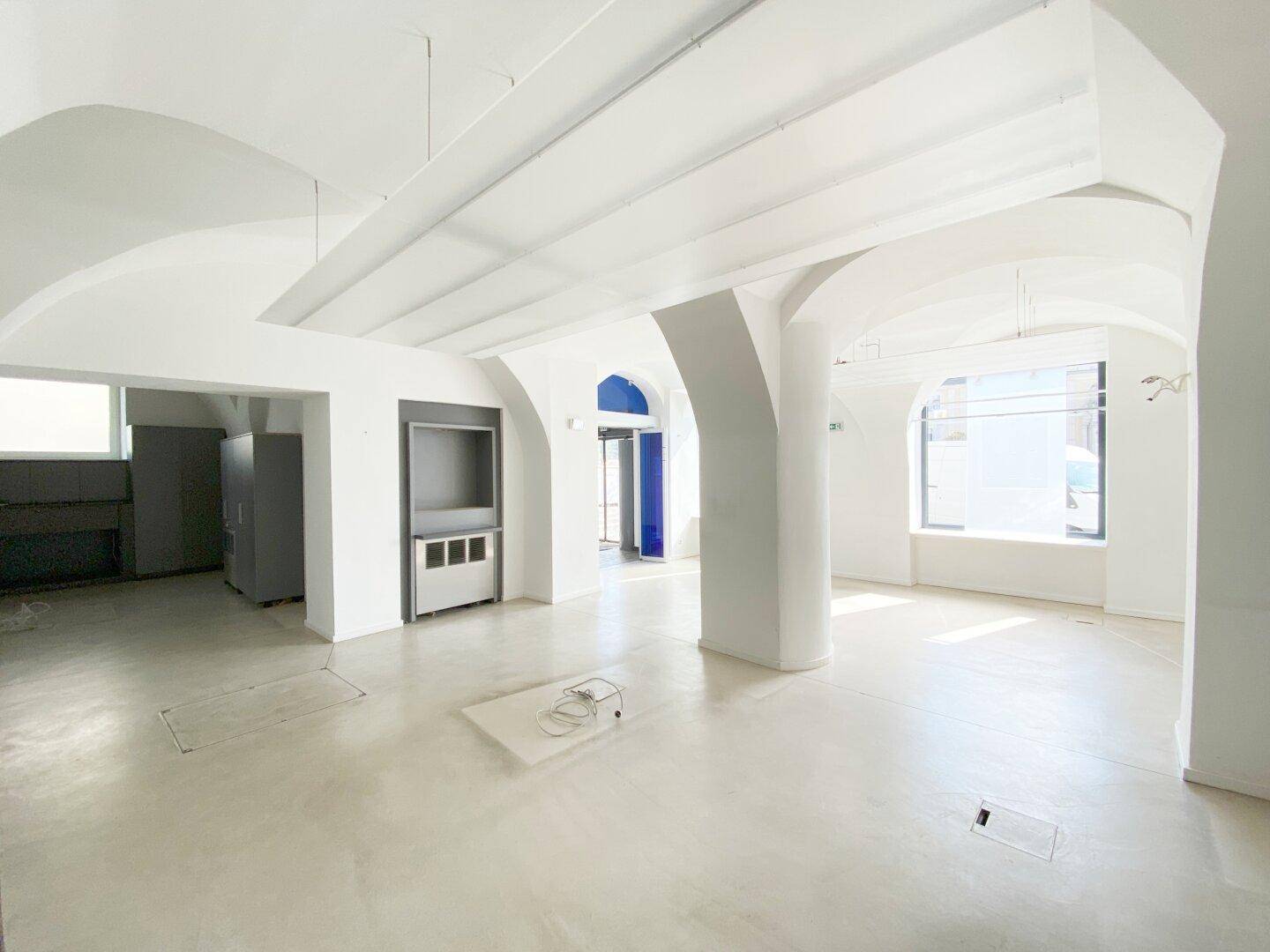 Heller, offener Gewerberaum mit Gewölbedecken, Säulen und einem Bereich mit grauen Einbauschränken.