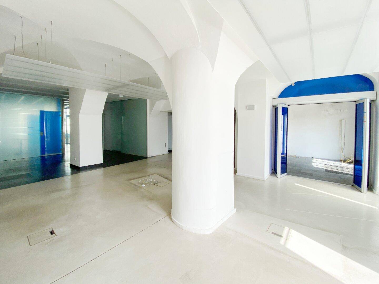 Geräumiger, leerer Gewerberaum mit hohen Gewölbedecken, hellen Fliesenböden und blauen Akzenten an den Türen.