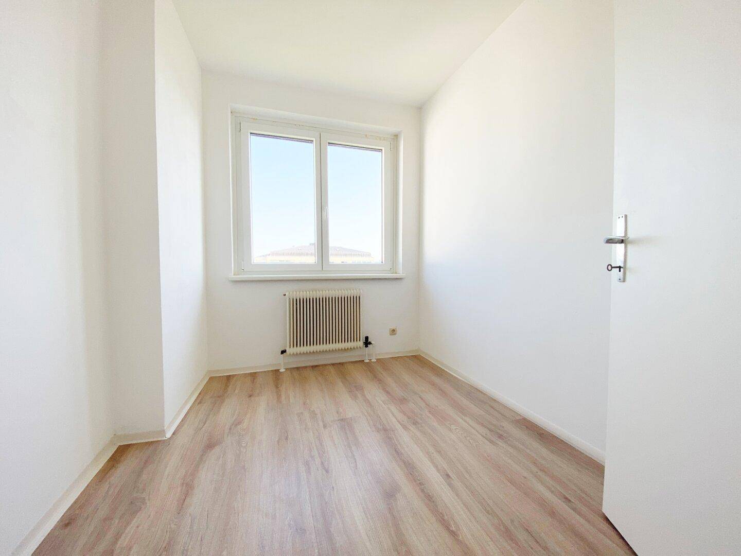 Kleineres Zimmer mit Laminatboden, Fenster und weißer Tür, vielseitig nutzbar als Kinder- oder Gästezimmer.