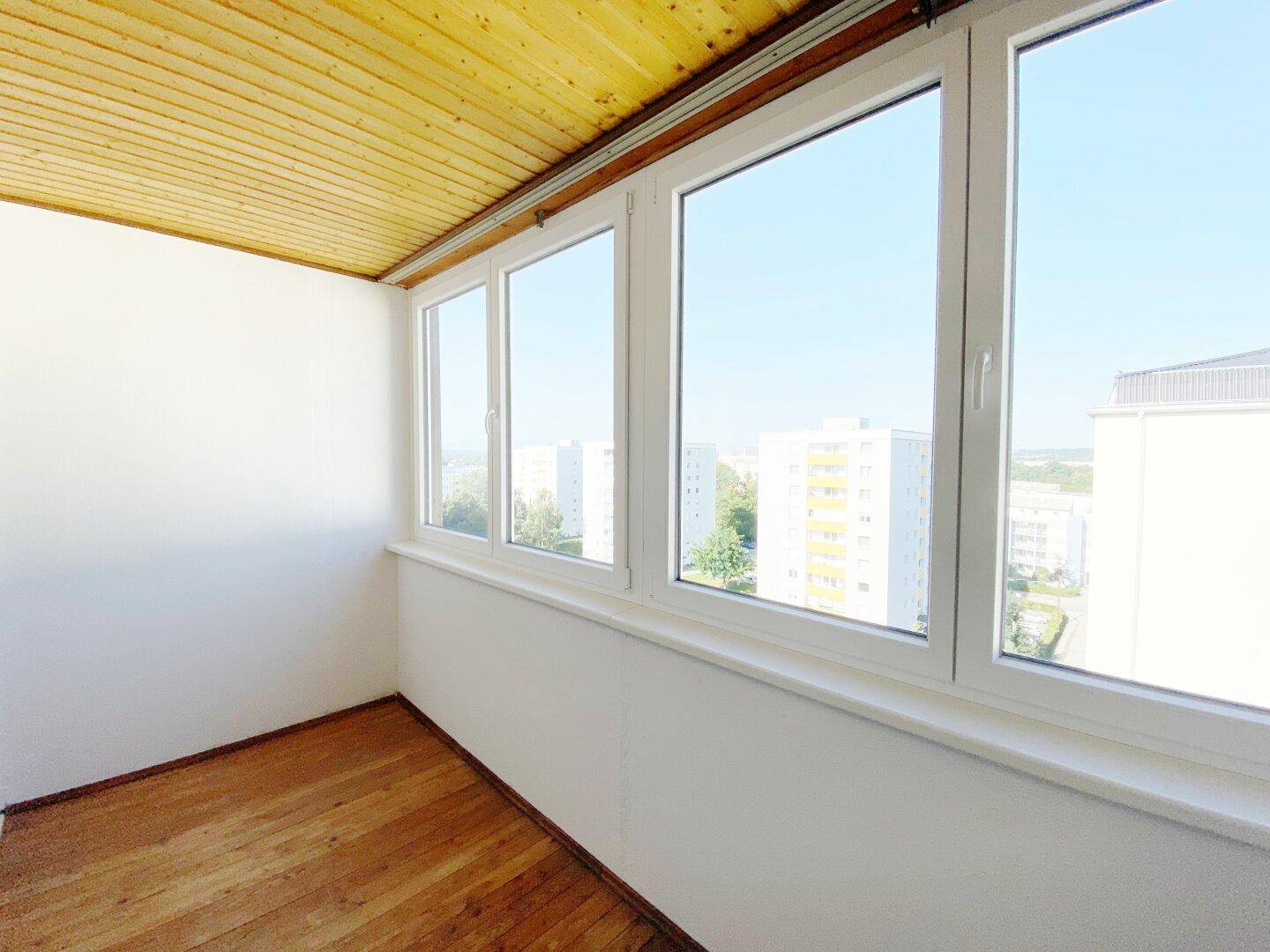 Verglaste Loggia mit Holzdecke und weitem Blick über die umliegenden Wohngebäude der Stadt.