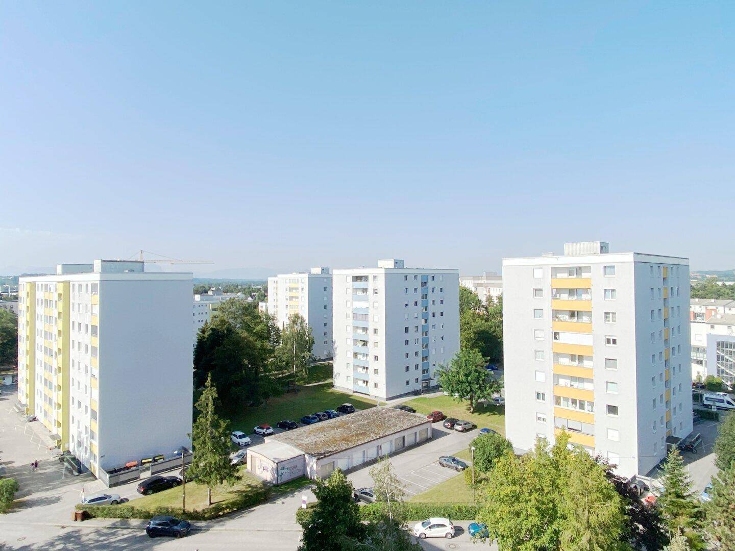 Weitläufige Ansicht einer Wohnsiedlung mit mehreren Mehrfamilienhäusern, Parkplätzen und Grünflächen.