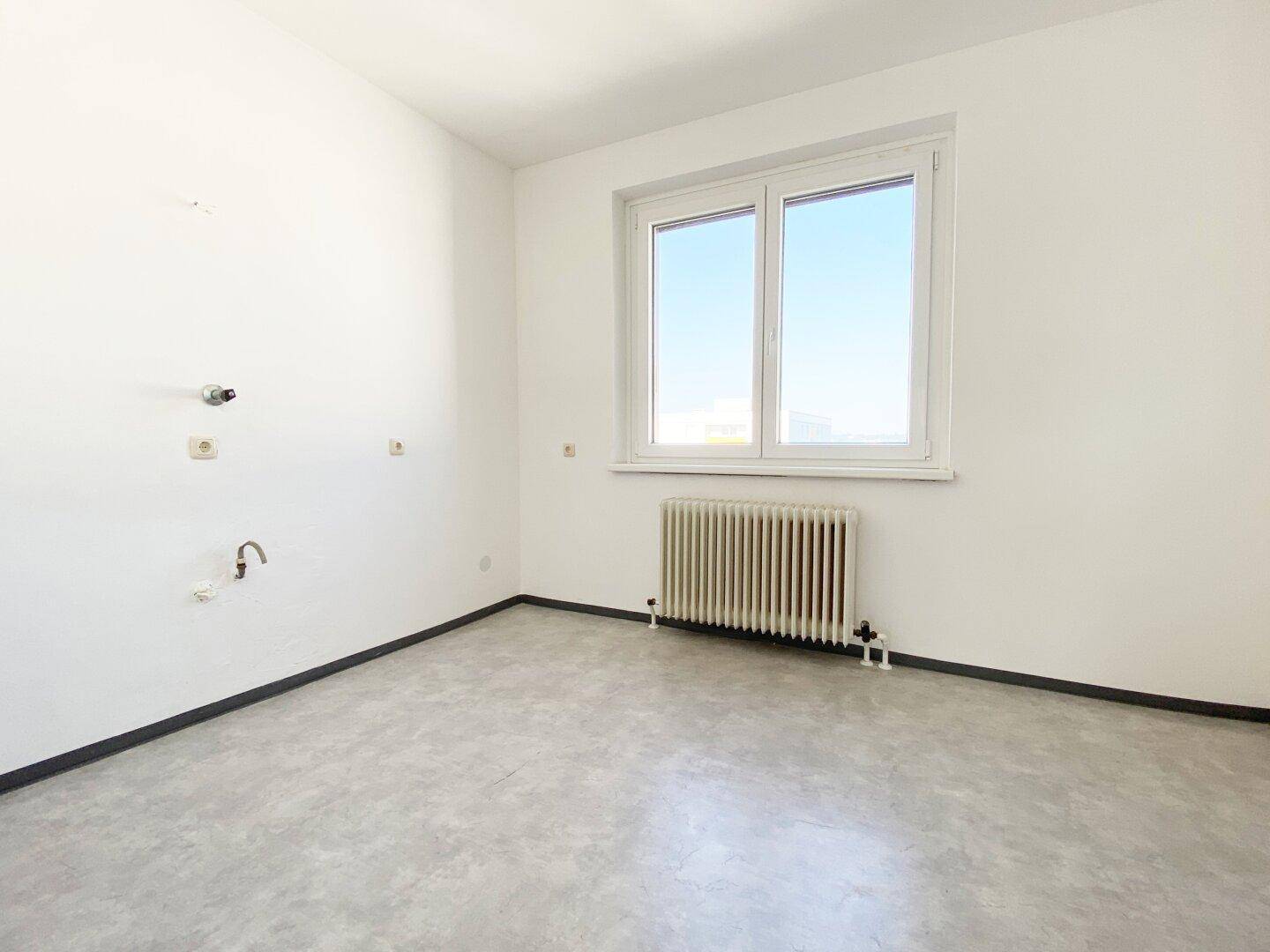 Leerer Raum, vorbereitet als Küche, mit Anschlüssen, Fenster und grauem Vinylboden.