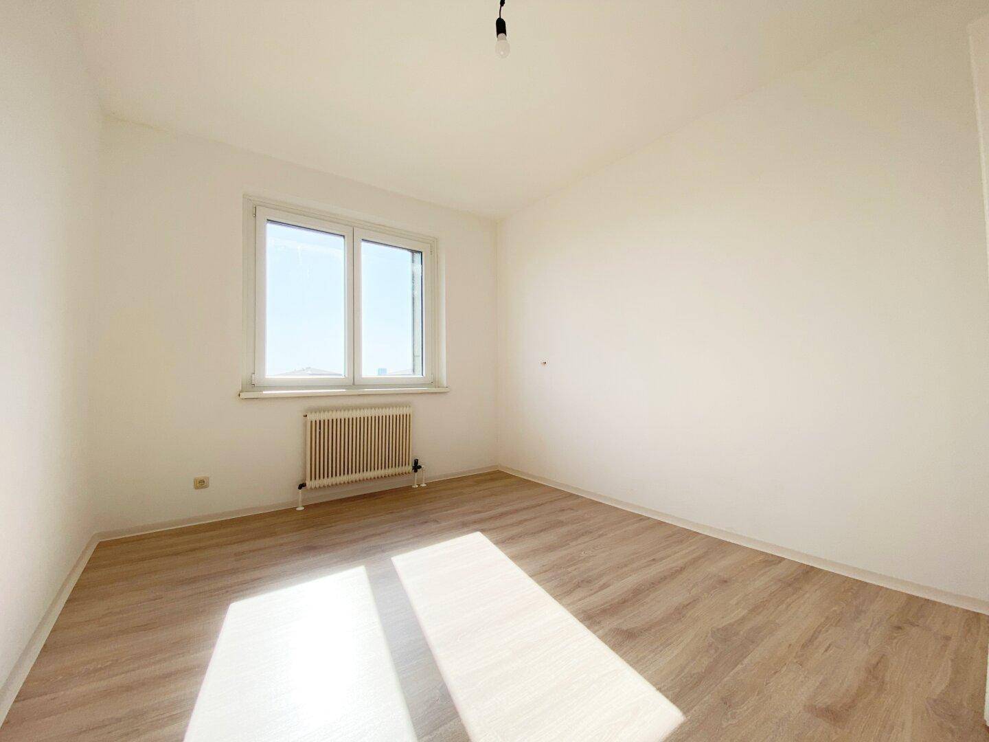 Sonniger Raum mit Laminatboden und Fenster, viel Tageslicht fällt auf den Boden.