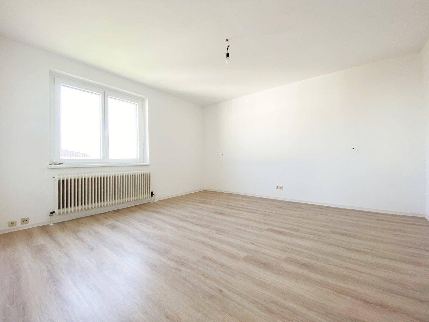 Helles Zimmer mit Laminatboden, großem Fenster und Heizkörper, ideal als Schlaf- oder Arbeitszimmer.