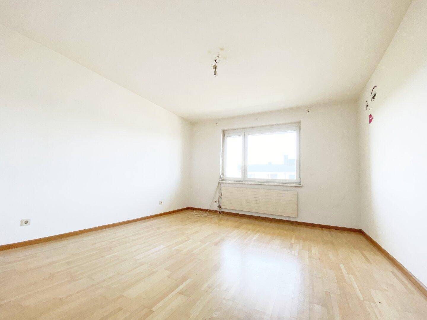 Helles, leeres Zimmer mit Parkettboden und weiß gestrichenen Wänden, bereit zur individuellen Gestaltung.