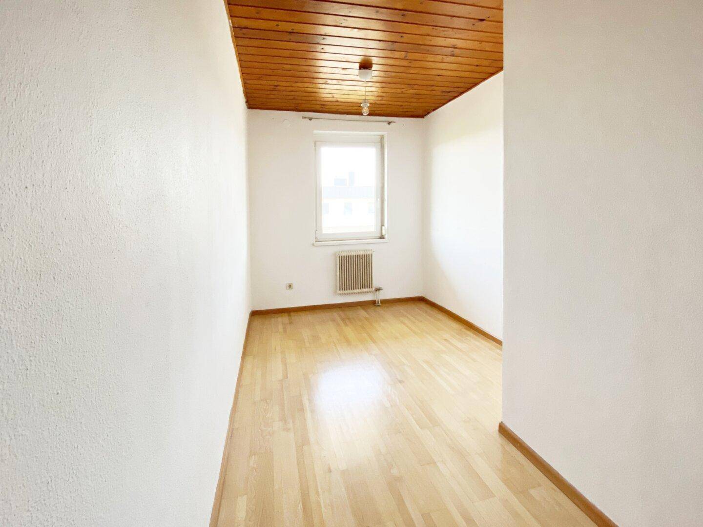 Kleines, helles Zimmer mit Parkettboden, weiß gestrichenen Wänden und Holzdeckenverkleidung.