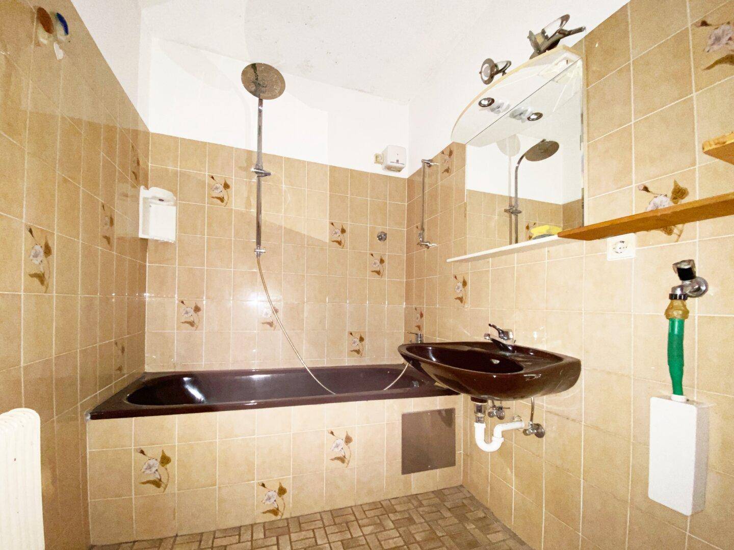 Badezimmer im Stil der 80er Jahre mit braunen Fliesen, Badewanne und passendem Waschbecken.