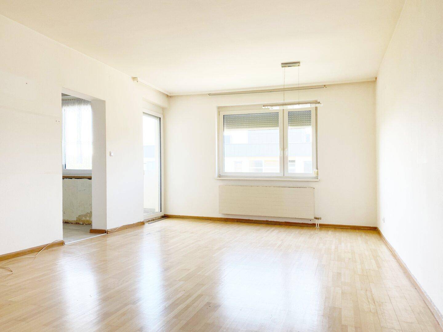 Geräumiges Zimmer mit Parkettboden, großen Fenstern und Zugang zu einem weiteren Bereich.