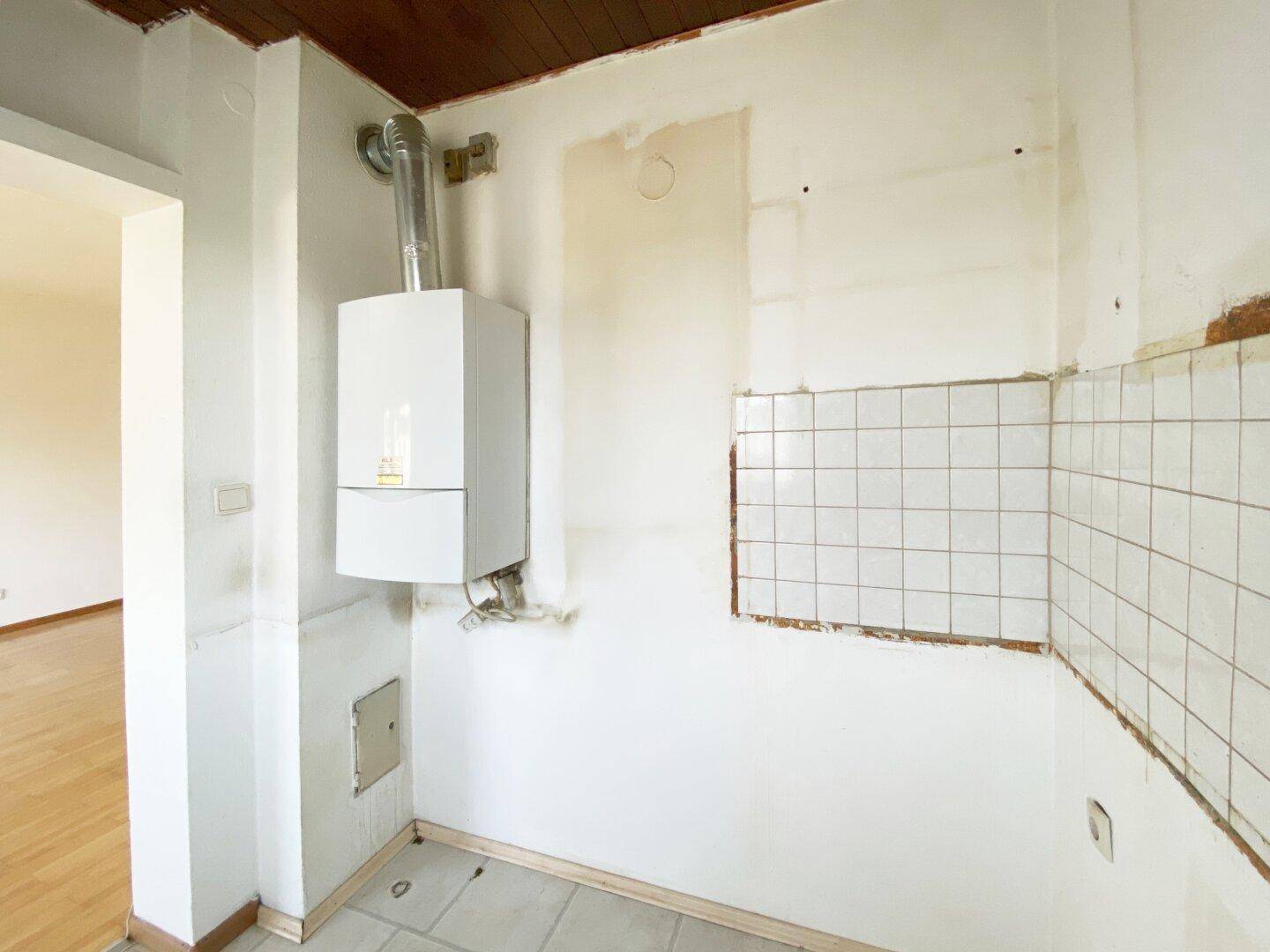 Renovierungsbedürftige Küche mit Gastherme, teilweise gefliesten Wänden und Holzdeckenverkleidung.