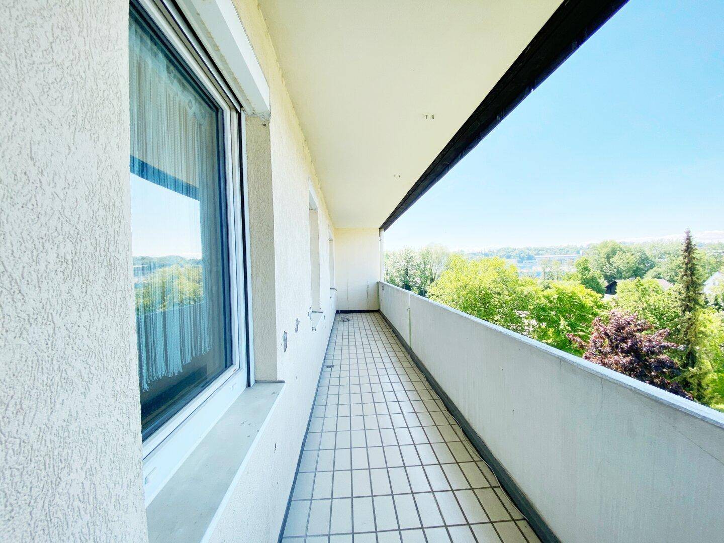 Langer Balkon mit Fliesenboden und weitem Blick ins Grüne und auf die Umgebung.