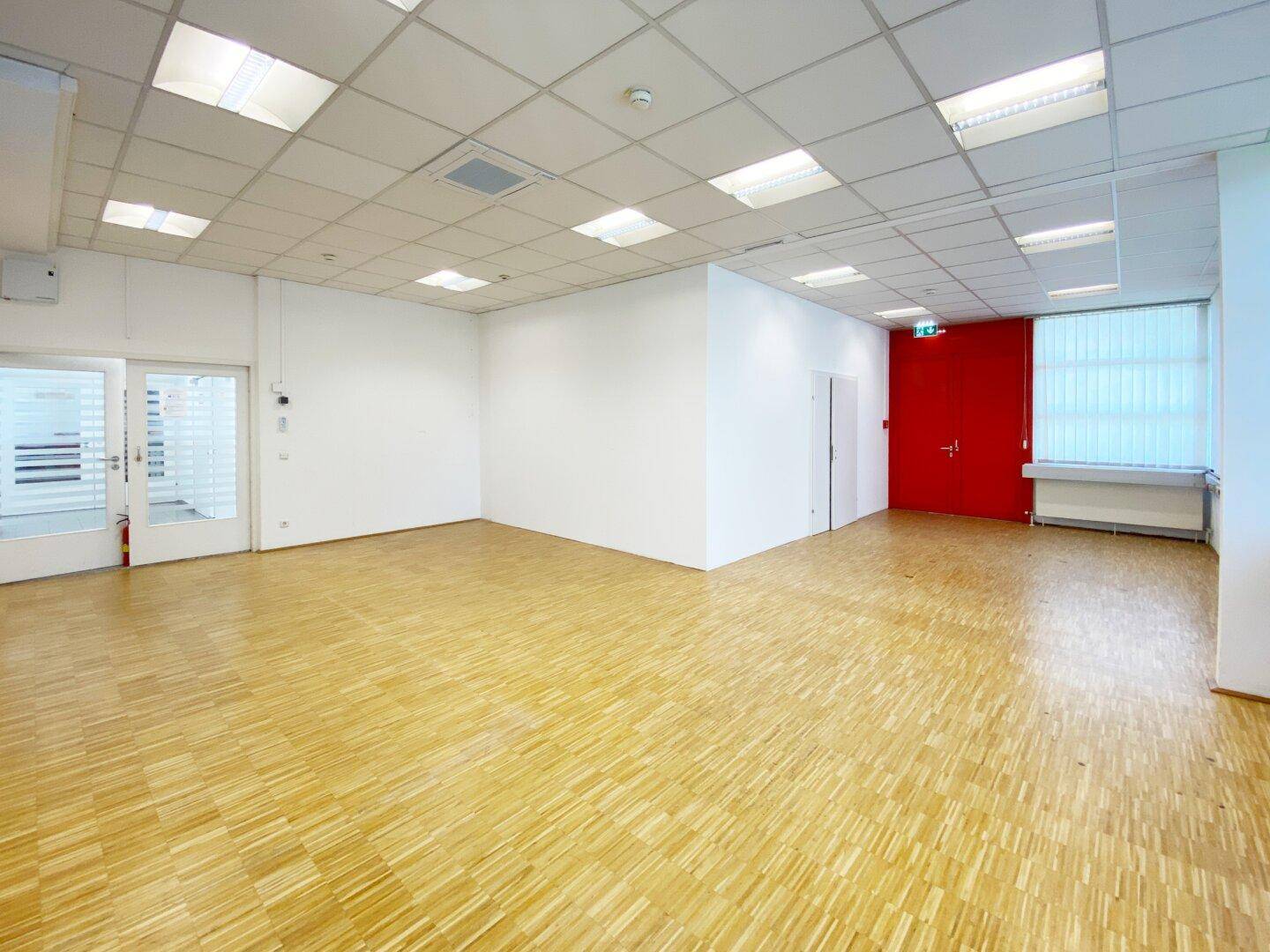 Leeres Büro mit hellem Parkettboden und einer auffälligen roten Tür.