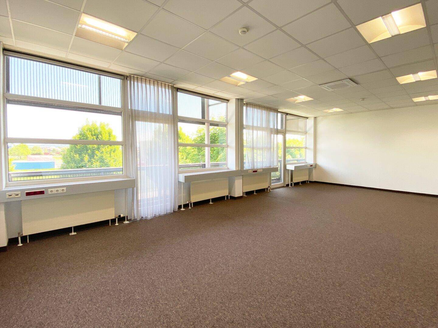 Geräumiges Büro mit Teppichboden und großen Fenstern, die einen weiten Blick bieten.