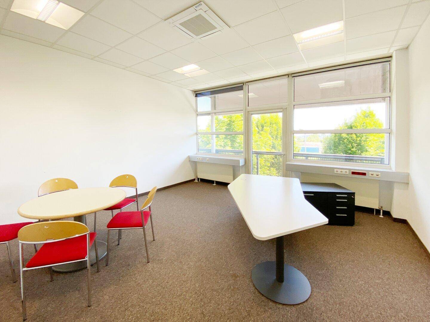 Büro mit runden Tischen und Stühlen, großen Fenstern und Teppichboden.