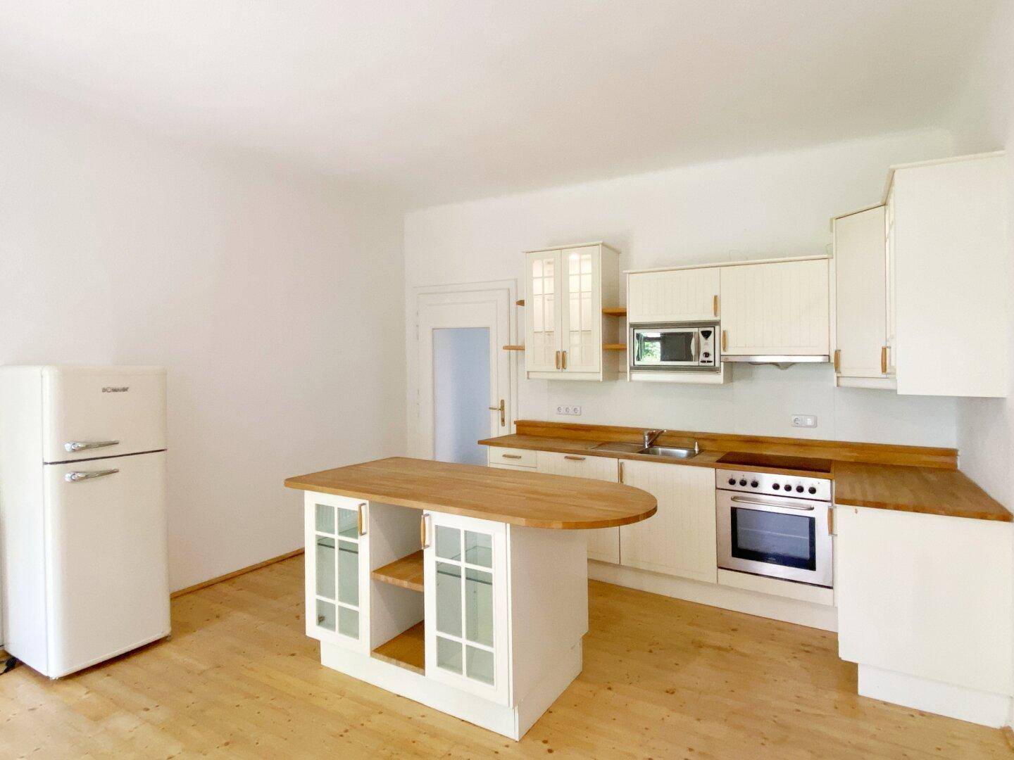 Klassische Küche mit weißen Schränken, Holztheke und freistehendem Kühlschrank.