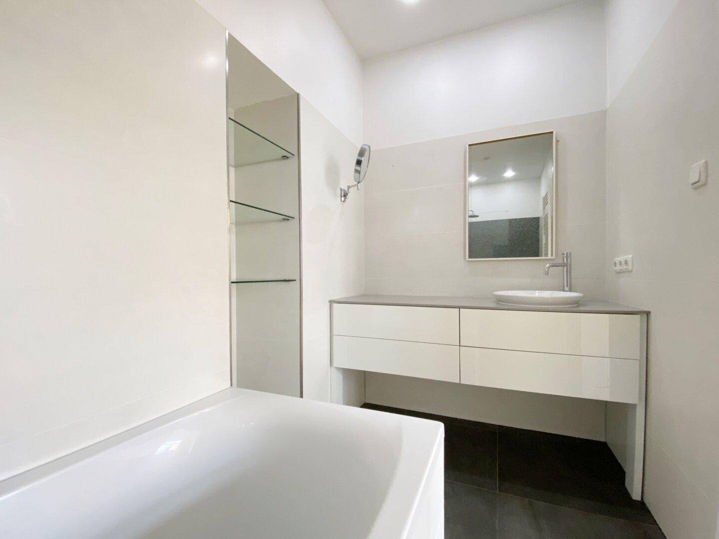 Modernes Badezimmer mit Badewanne, Waschtisch, großem Spiegel und eleganten Fliesen.