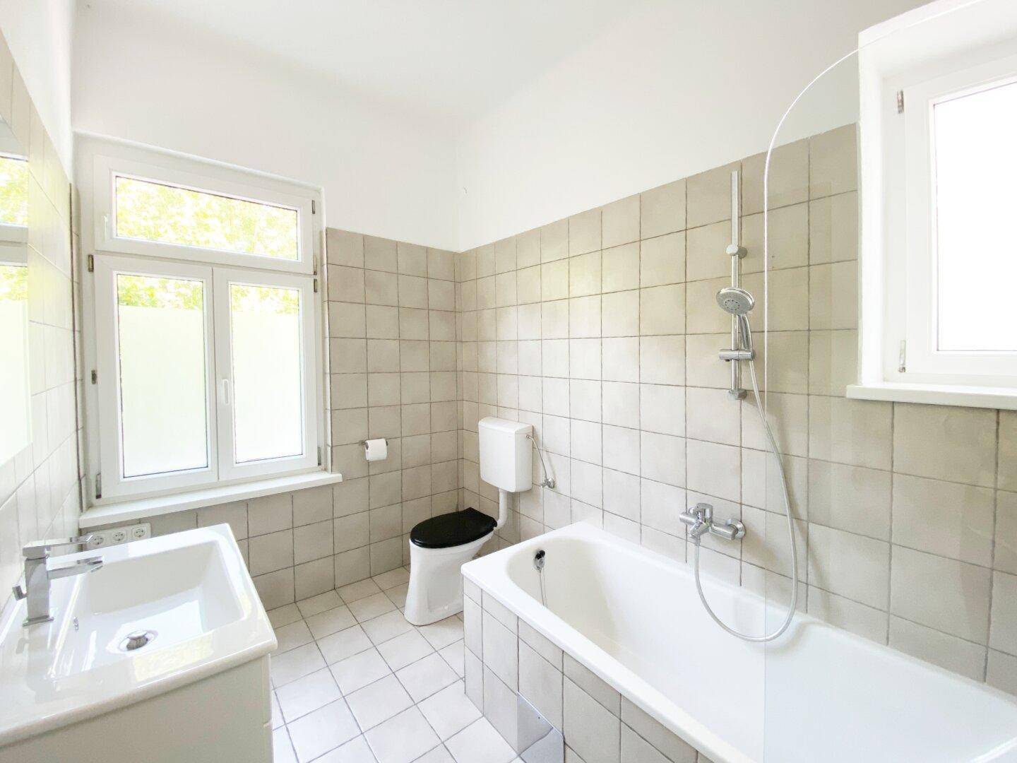 Helles Badezimmer mit Badewanne, WC, Waschbecken und Fenster, komplett gefliest in hellen Tönen.