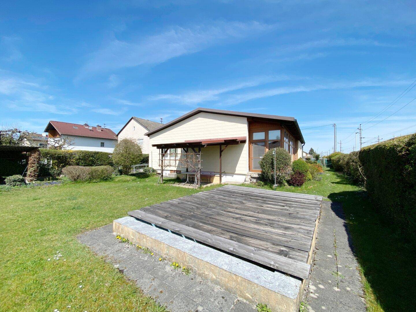 Weitläufiger Gartenbereich mit Holzterrasse und überdachtem Sitzplatz.